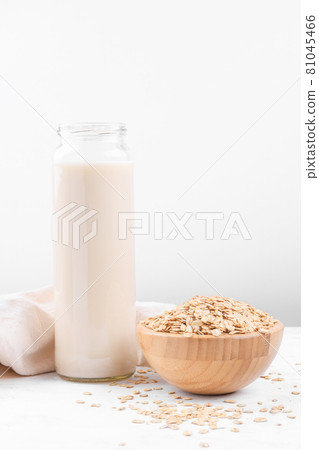 Oat milk in a bottle and a bowl with oat flake on white table Oat milk in a bottle and a bowl with oat flake on white table 81045466
