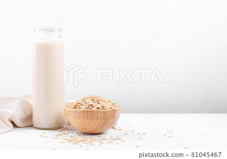 Oat milk in a bottle and a bowl with oat flake on white table Oat milk in a bottle and a bowl with oat flake on white table 81045467