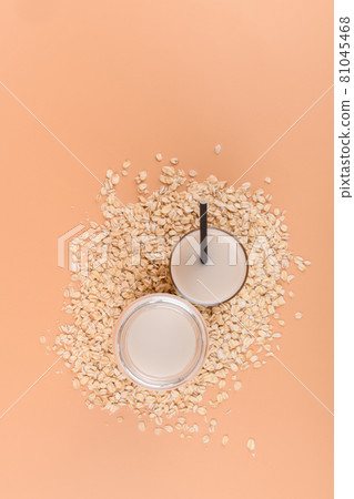 bottle and glass with oat milk on the oat flake on pastel peach color background bottle and glass with oat milk on the oat flake on pastel peach color background 81045468