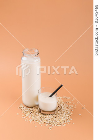 Oat milk in bottle and glass on the oat flake on pastel peach color background Oat milk in bottle and glass on the oat flake on pastel peach color background 81045469