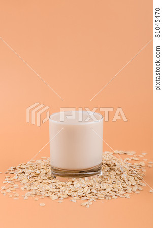 Oat milk in a glass on the oat flake on pastel peach color background Oat milk in a glass on the oat flake on pastel peach color background 81045470