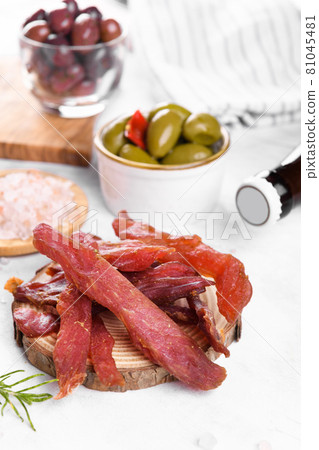 Jerky meat strips with spices, olives, snack for beer on wooden plate Jerky meat strips with spices, olives, snack for beer on wooden plate 81045481