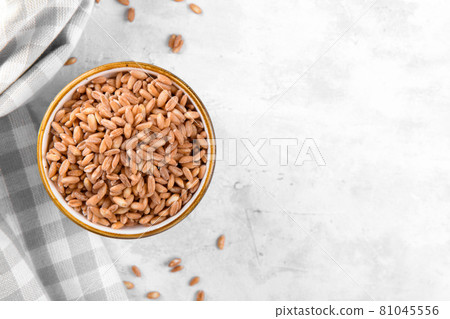 Wholegrain uncooked raw spelt farro in ceramic bowl with napkin on grey table Wholegrain uncooked raw spelt farro in ceramic bowl with napkin on grey table 81045556