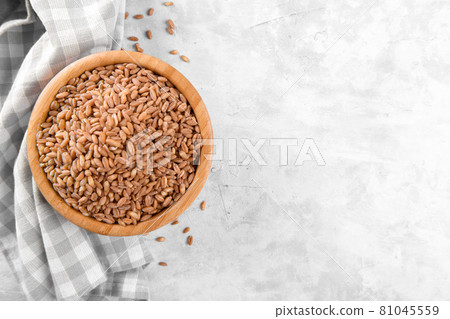 Wholegrain uncooked raw spelt farro in wooden bowl on grey stone table 81045559