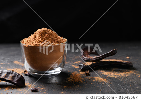 Dry carob pods and carob powder over dark background Dry carob pods and carob powder over dark background 81045567