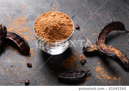 Dry carob pods and carob powder over dark background Dry carob pods and carob powder over dark background 81045568