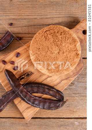 Dry carob pods and carob powder over wooden background 81045581