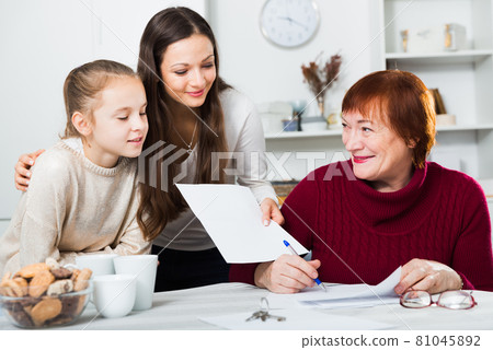 Smiling woman with girl helping elderly mother with paperwork 81045892