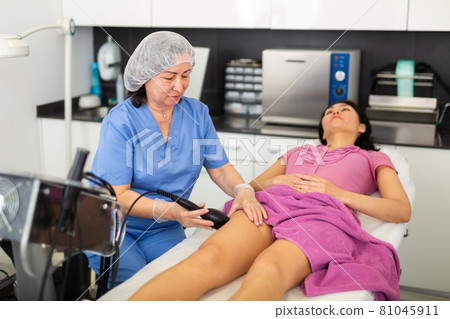 Mature beautician performing machine cosmetological procedure to female in cosmetic clinic Mature beautician performing machine cosmetological procedure to female in cosmetic clinic 81045911