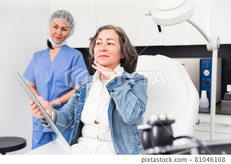 Happy elderly woman examining face after cosmetology procedures 81046108