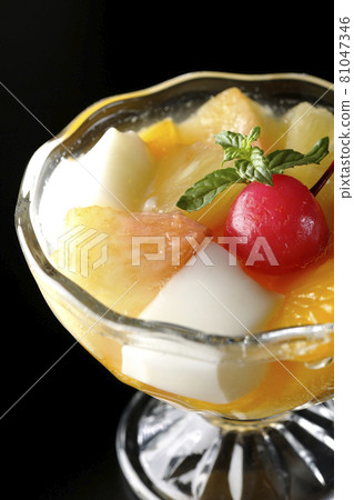 Photographed a fruit punch containing fruits such as milk cans, pineapples, mangoes, white peaches, cherries, and oranges on a black background. 81047346