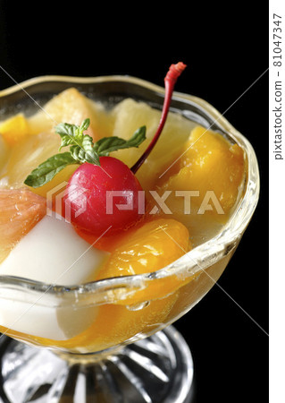 在黑色背景上拍攝了一種水果潘趣酒，裡面裝著牛奶罐、菠蘿、芒果、白桃、櫻桃和橙子等水果。 81047347