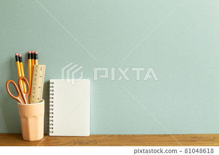 White notebook and pencils, ruler and scissors in holder on wooden desk. blue wall background. workspace White notebook and pencils, ruler and scissors in holder on wooden desk. blue wall background. workspace 81048618