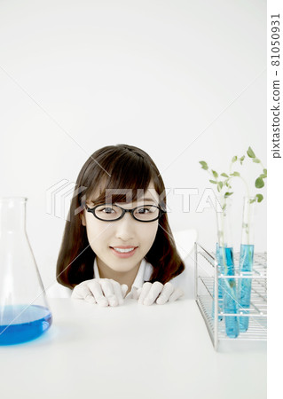 A close-up of the face of a young woman looking at the camera, smiling sideways with a test tube and flask in the laboratory. 81050931