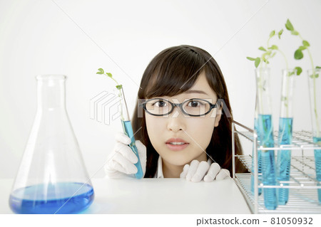 一個年輕女子的臉特寫，看著相機，在實驗室裡用試管和燒瓶側身微笑。 81050932