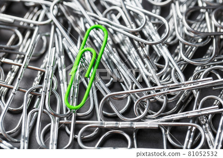 The green paper clip stands out against a textured background of silver paper clips The green paper clip stands out against a textured background of silver paper clips 81052532
