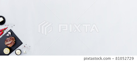 Gray background flat lay with cut of red rib-eye meat on black cutting board Gray background flat lay with cut of red rib-eye meat on black cutting board 81052729