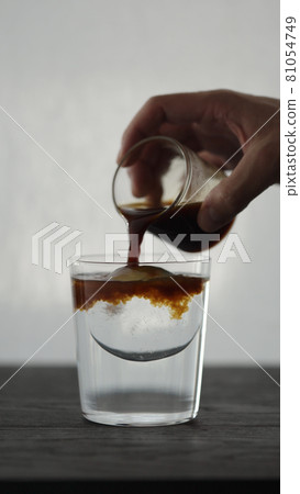Vertical shot of making espresso tonic in tumbler glass, pour espresso over ice ball 81054749