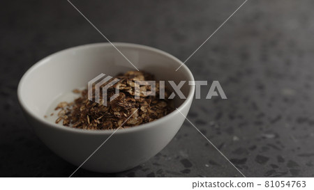 Pour granola over yogurt in white bowl 81054763