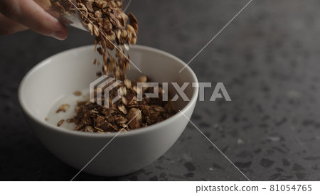 Pour granola over yogurt in white bowl 81054765