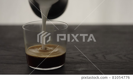 Pour steamed milk into espresso in tumbler glass on oak table with copy space Pour steamed milk into espresso in tumbler glass on oak table with copy space 81054776