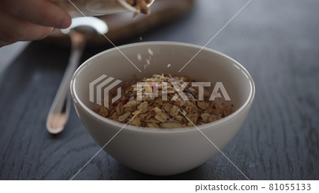Pour granola over yogurt in white bowl 81055133
