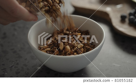 pour granola over yogurt in white bowl 81055182