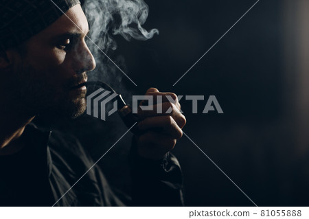 Man smoking a pipe on dark background. Back lit profile portrait. Man smoking a pipe on dark background. Back lit profile portrait. 81055888
