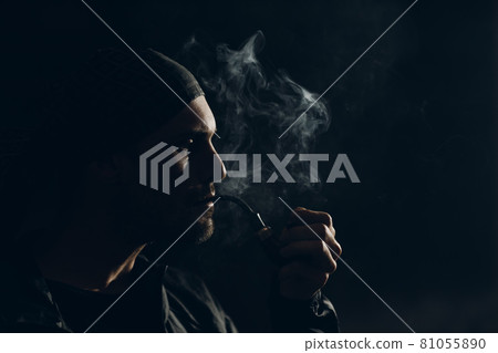 Man smoking a pipe on dark background. Back lit profile portrait. Man smoking a pipe on dark background. Back lit profile portrait. 81055890