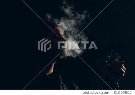 Man smoking a pipe on dark background. Back lit profile portrait. 81055903