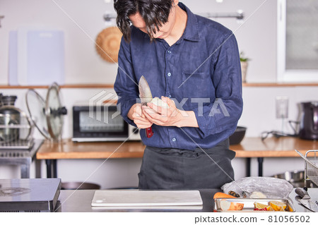 A young man in an apron who cuts onions with a kitchen knife. A young man in an apron who cuts onions with a kitchen knife. 81056502