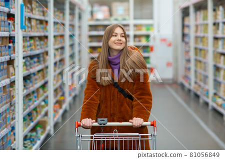 Young woman with grocery cart and shelves with groceries in a store. Young woman with grocery cart and shelves with groceries in a store. 81056849