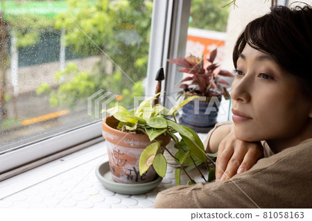 A woman looking at the rainy city by the window 81058163