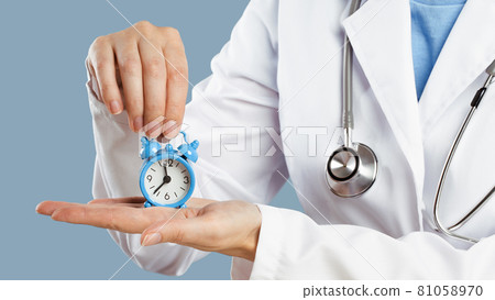 Doctors hands holding an alarm clock over blue background 81058970