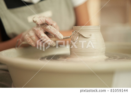 Potter with tool shaping clay vessel 81059144