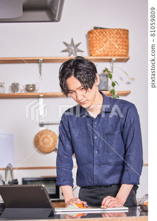 Image of a young man cooking in an apron who cooks while looking at the recipe on a tablet Image of a young man cooking in an apron who cooks while looking at the recipe on a tablet 81059809