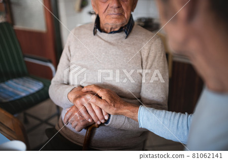 Unrecognizable man with elderly father sitting at the table indoors at home, talking. 81062141