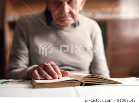 Portrait of elderly man sitting at the table indoors at home, resting and reading bible. 81062142