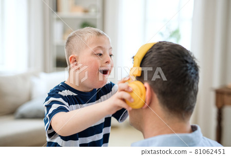 Happy down syndrome boy with father indoors at home, having fun with headphones. 81062451