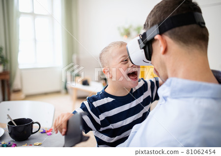 Father with happy down syndrome son indoors at home, using vr goggles. 81062454