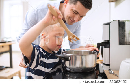 Father with happy down syndrome son indoors in kitchen, cooking. 81062462