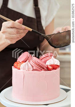 Woman pastry chef decorates pink cake with macaroons and berries, close-up. Cake making process, Selective focus 81062575