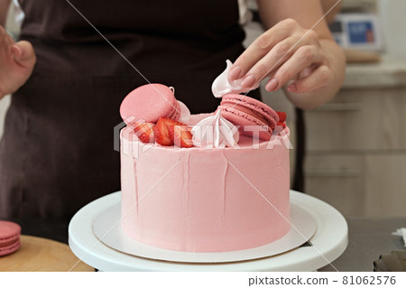 Woman pastry chef decorates pink cake with macaroons and berries, close-up. Cake making process, Selective focus 81062576