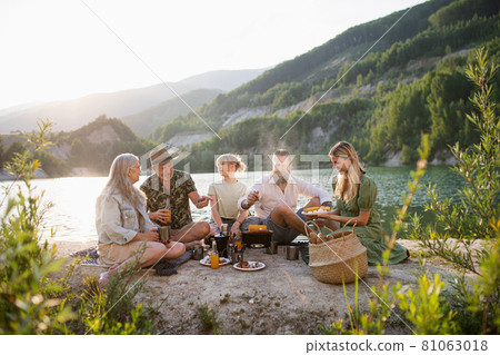 Happy multigeneration family on summer holiday trip, barbecue by lake. 81063018