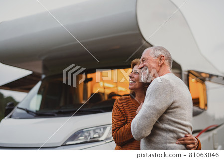 Senior couple standing and hugging outdoors at dusk, caravan holiday trip. 81063046