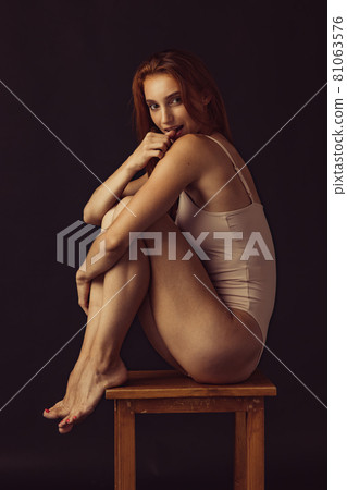 Portrait of young beautiful slim tanned red headed woman in lingerie posing isolated over dark studio background. Natural beauty concept. Portrait of young beautiful slim tanned red headed woman in lingerie posing isolated over dark studio background. Natural beauty concept. 81063576