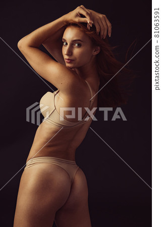 Half length portrait of young beautiful slim tanned red headed woman in lingerie posing isolated over dark studio background. Natural beauty concept. 81063591