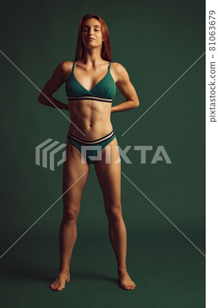 Full length portrait of young beautiful slim tanned red headed woman in lingerie posing isolated over green studio background. Natural beauty concept. 81063679