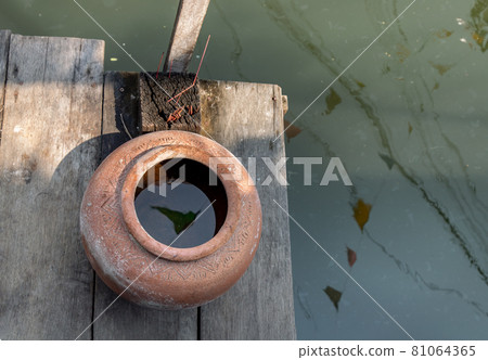Old big earthen jar or Vintage clay jar for water storage on pier waterfront balcony pavilion at thai ancient style house. Old big earthen jar or Vintage clay jar for water storage on pier waterfront balcony pavilion at thai ancient style house. 81064365