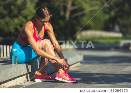 One young slim sportive caucasian woman in bright sportswear sitting in the park or on city street. One young slim sportive caucasian woman in bright sportswear sitting in the park or on city street. 81064373